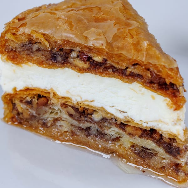 Close-up of a slice of Greek baklava with a creamy white filling and honey drizzle.
