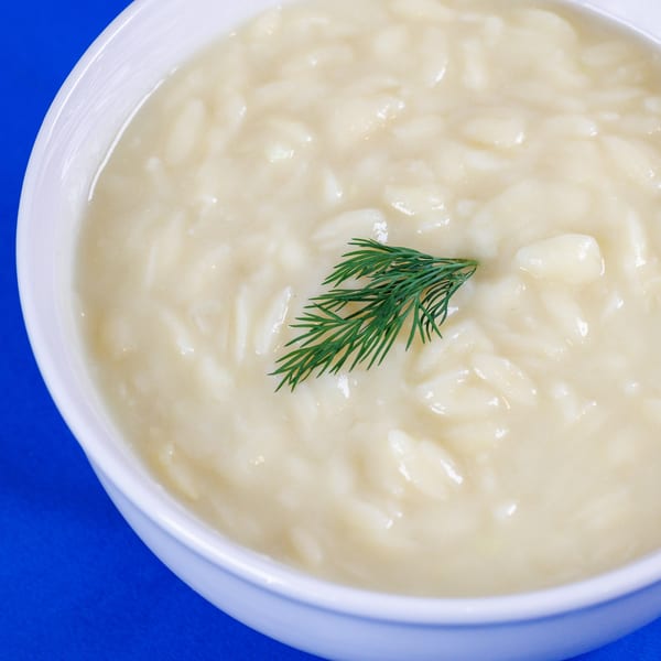 Creamy Greek orzo pasta in a white bowl, garnished with a sprig of fresh dill.
