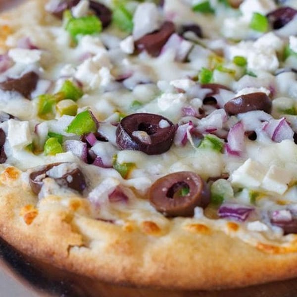 Close-up of a Greek pizza with olives, feta, red onions, and green peppers.