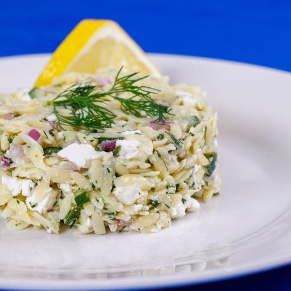 Orzo pasta salad with feta, red onion, and dill, garnished with a lemon wedge.