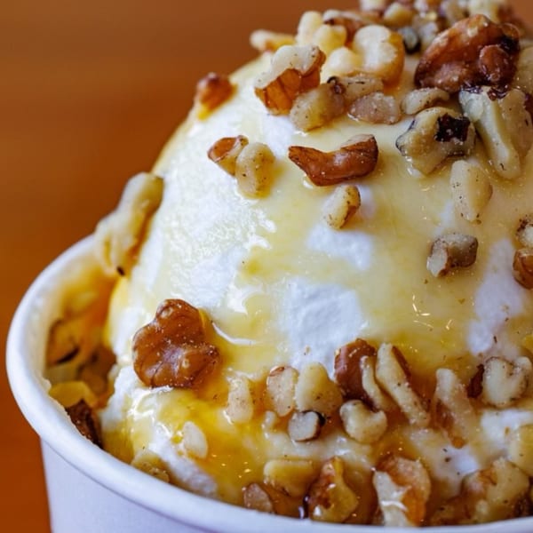 Close-up of Greek yogurt with honey and walnuts in a white cup.