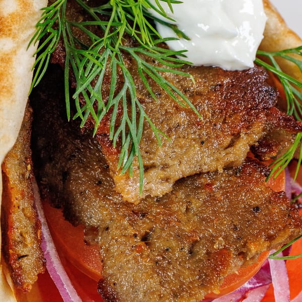 Close-up of a Freskos Greek gyro with sliced meat, tomatoes, red onions, dill, and tzatziki.