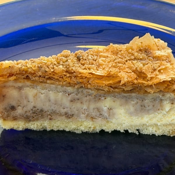 A slice of layered cake with a flaky, crumbly top and creamy filling on a blue plate.