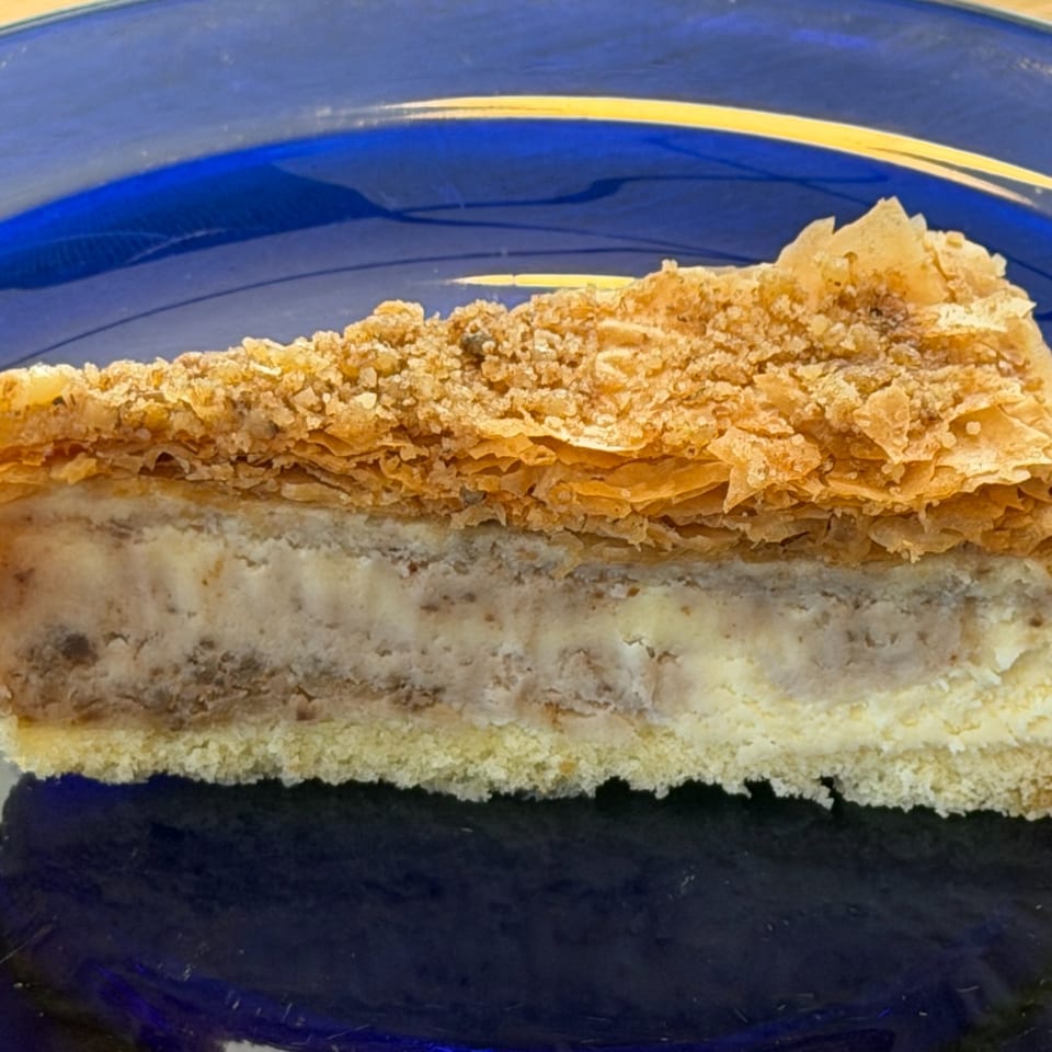 A slice of layered cake with a flaky, crumbly top and creamy filling on a blue plate.